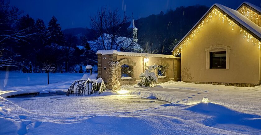Havas téli táj, vendégház épülete, karácsonyi világítással.