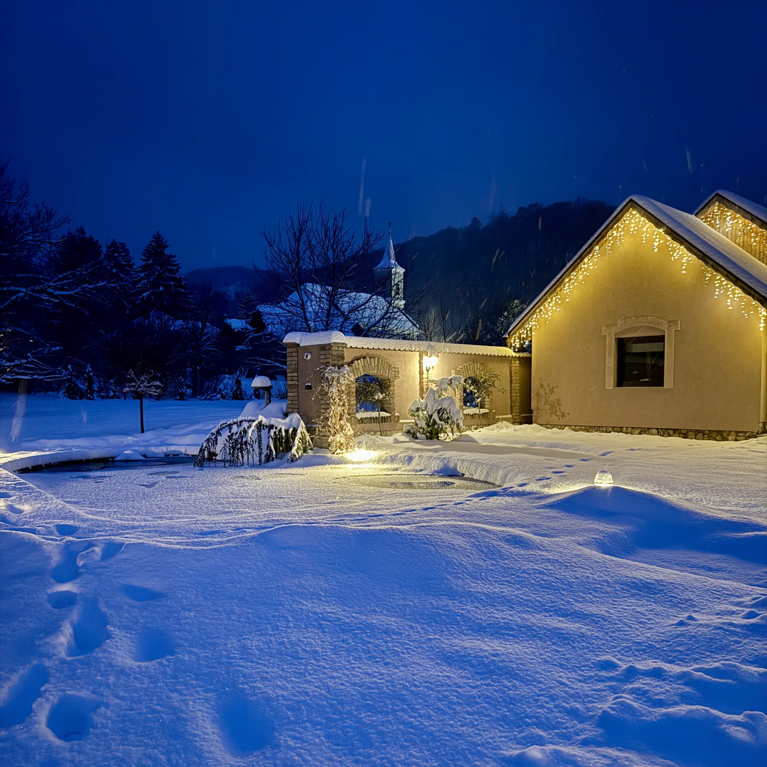 Havas téli táj, vendégház épülete, karácsonyi világítással.