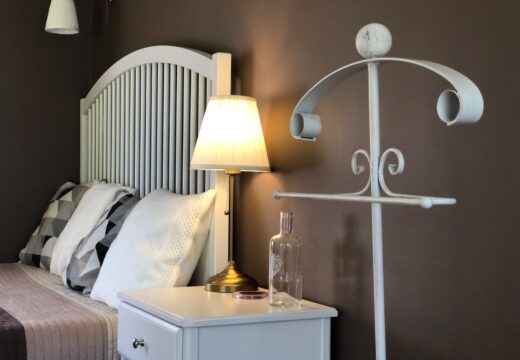 Fehér ágyvég, éjjeliszekrény és világító asztali lámpa a Tulipán Vendégház Romantik apartmanjában.