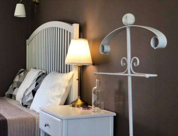 Fehér ágyvég, éjjeliszekrény és világító asztali lámpa a Tulipán Vendégház Romantik apartmanjában.