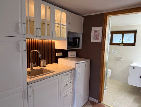 A kárászi Tulipán Vendégház Romantik apartmanjának konyhája fehér szekrényekkel, mosogatóval és hűtővel.