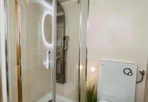 Íves üvegajtós zuhanykabin és WC a Romantik apartman világos fürdőszobájában.