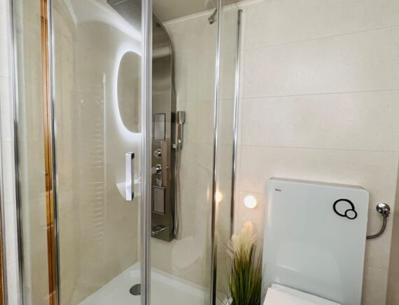 Íves üvegajtós zuhanykabin és WC a Romantik apartman világos fürdőszobájában.
