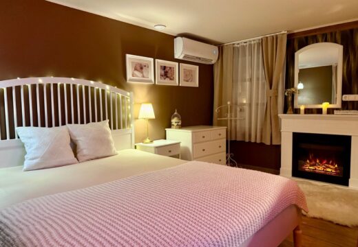 Franciaágy rózsaszín ágytakaróval és világító látványkandalló a Romantik apartmanban.