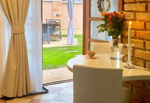 A Romantik apartman reggelizőasztala kávécsészével és virágcsokorral, a kertre nyíló ajtó mellett.