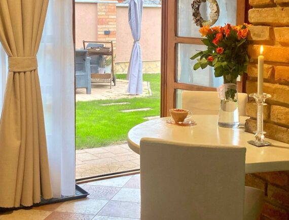 A Romantik apartman reggelizőasztala kávécsészével és virágcsokorral, a kertre nyíló ajtó mellett.
