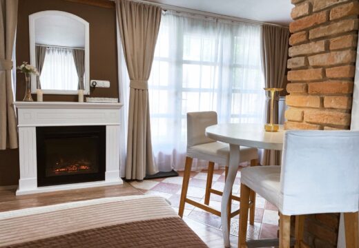 A Romantik apartman szobabelsője fehér kandallóval, tükörrel és ablak melletti reggelizőasztallal.