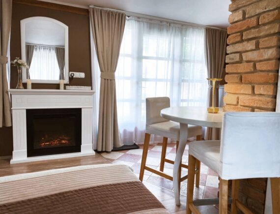 A Romantik apartman szobabelsője fehér kandallóval, tükörrel és ablak melletti reggelizőasztallal.