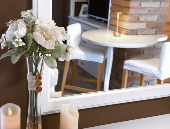 Fehér virágcsokor és gyertyák a Romantik apartman tükrénél, a tükörben a reggelizősarokkal.
