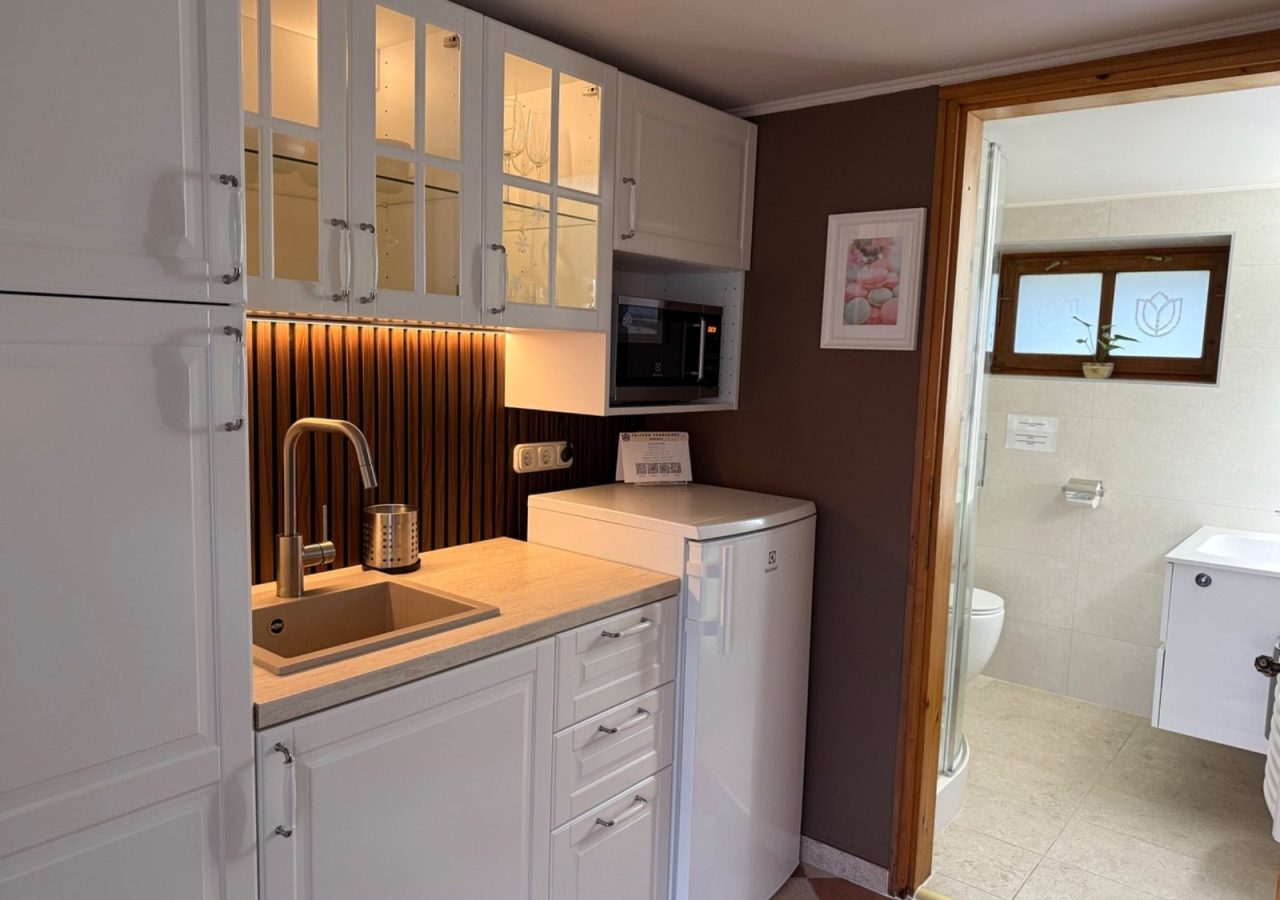 A kárászi Tulipán Vendégház Romantik apartmanjának konyhája fehér szekrényekkel, mosogatóval és hűtővel.
