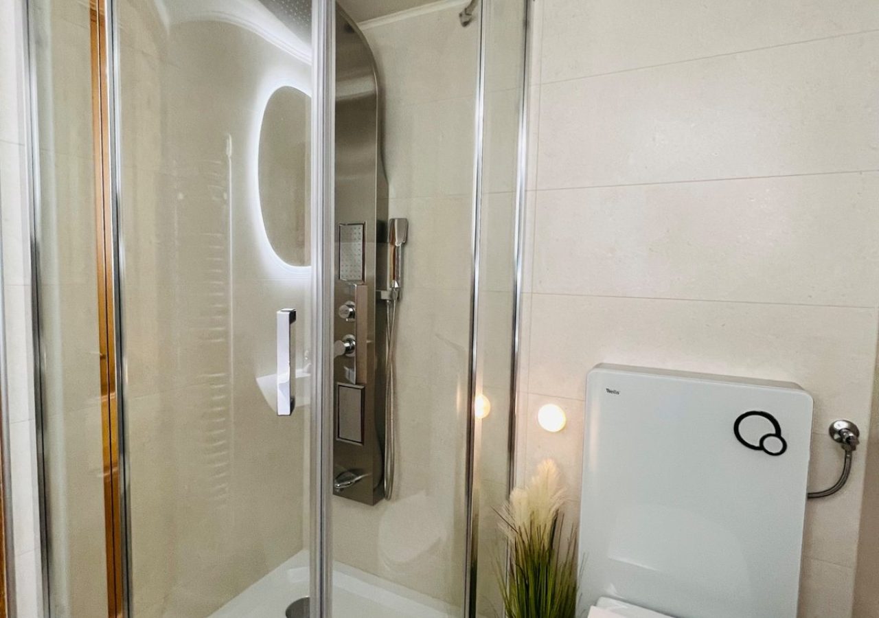 Íves üvegajtós zuhanykabin és WC a Romantik apartman világos fürdőszobájában.