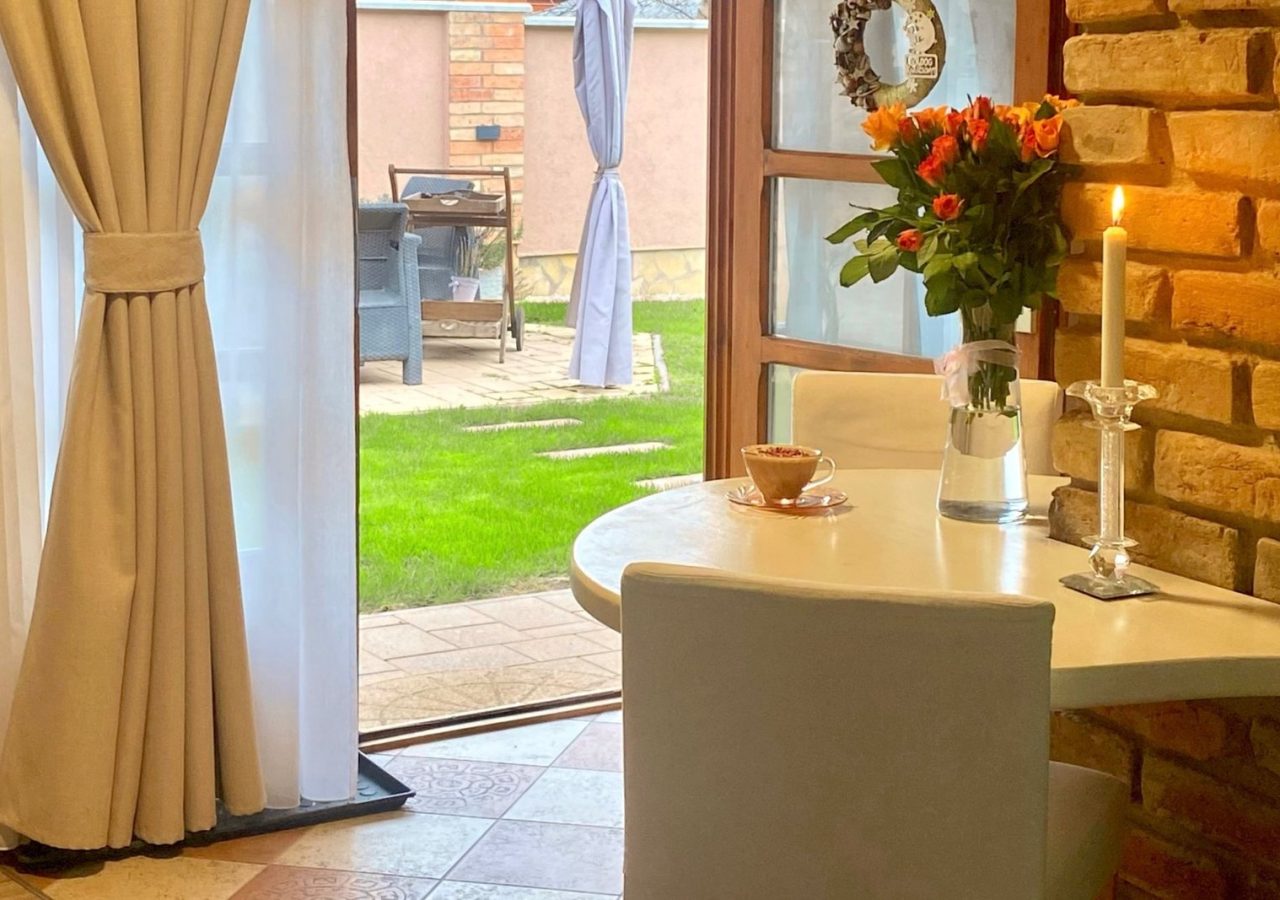 A Romantik apartman reggelizőasztala kávécsészével és virágcsokorral, a kertre nyíló ajtó mellett.